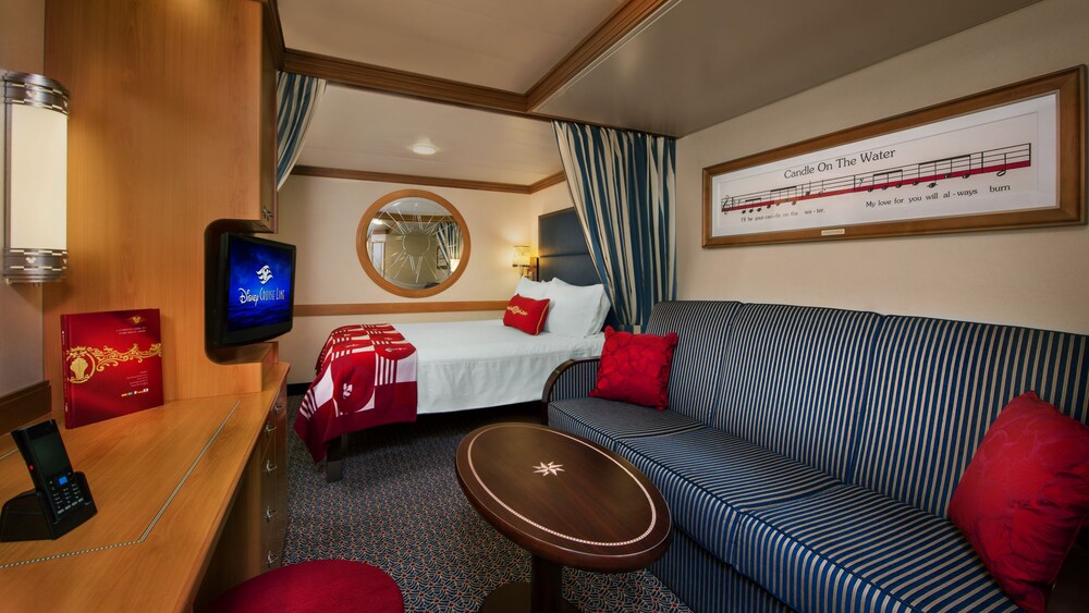 A Disney Cruise Line Deluxe Inside Stateroom with a bed, sofa, table, desk, TV and mirror