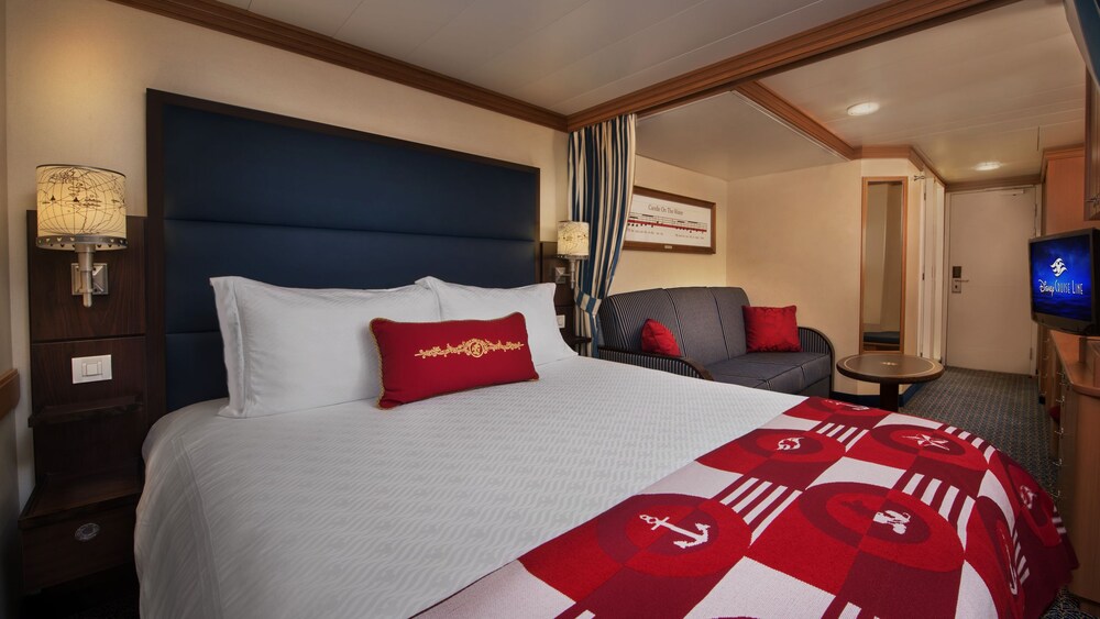 A Disney Cruise Line Deluxe Inside Stateroom with a bed, sofa, table, desk, mirror, TV and a nightstand