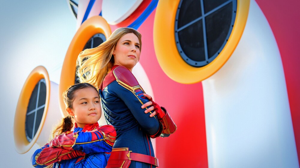 Captain Marvel standing back to back with a little girl in a similar costume on a Disney Cruise Line ship
