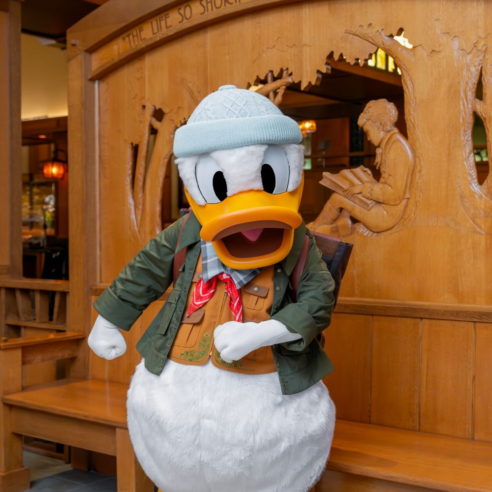 Donald Duck vestido con un atuendo para salir al aire libre cerca de un detallado banco de madera en Disney's Grand Californian Hotel & Spa