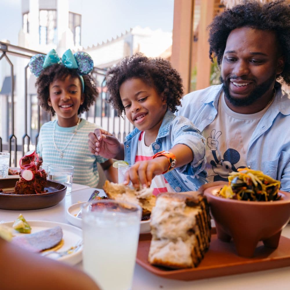 A family of 4 dining at a table in Paseo with a view of Disney Downtown District