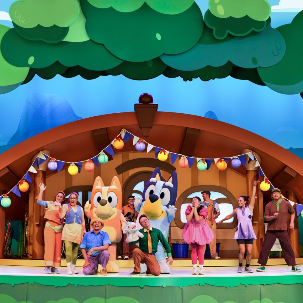 The cast of Bluey’s Best Day Ever pose on a stage set designed to look like a house in the woods