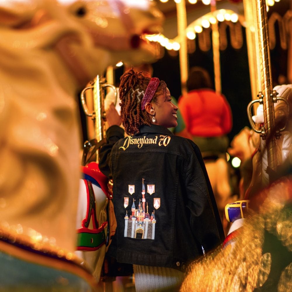 A Guest riding King Arthur Carrousel while wearing a Disneyland Resort 70th Celebration jacket