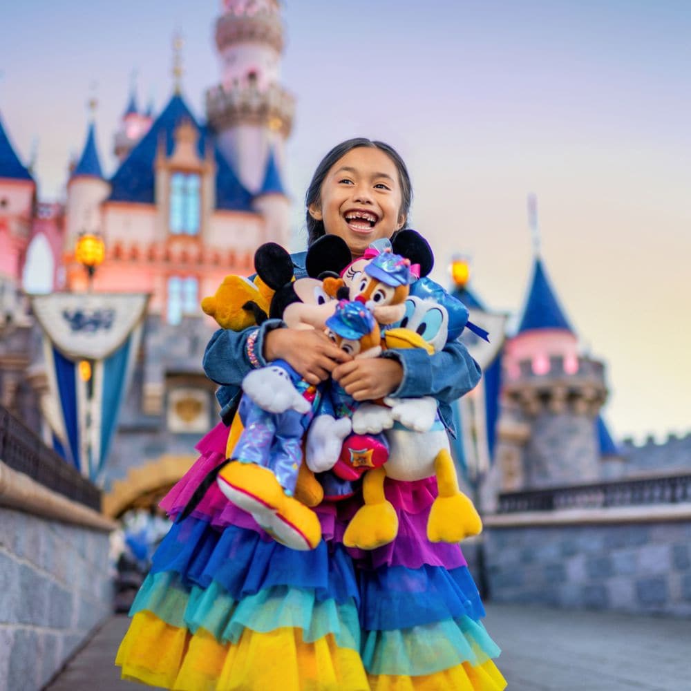 Una niña pequeña sostiene una colección de peluches de la Celebración del 70.º Aniversario del Disneyland Resort frente a Sleeping Beauty Castle