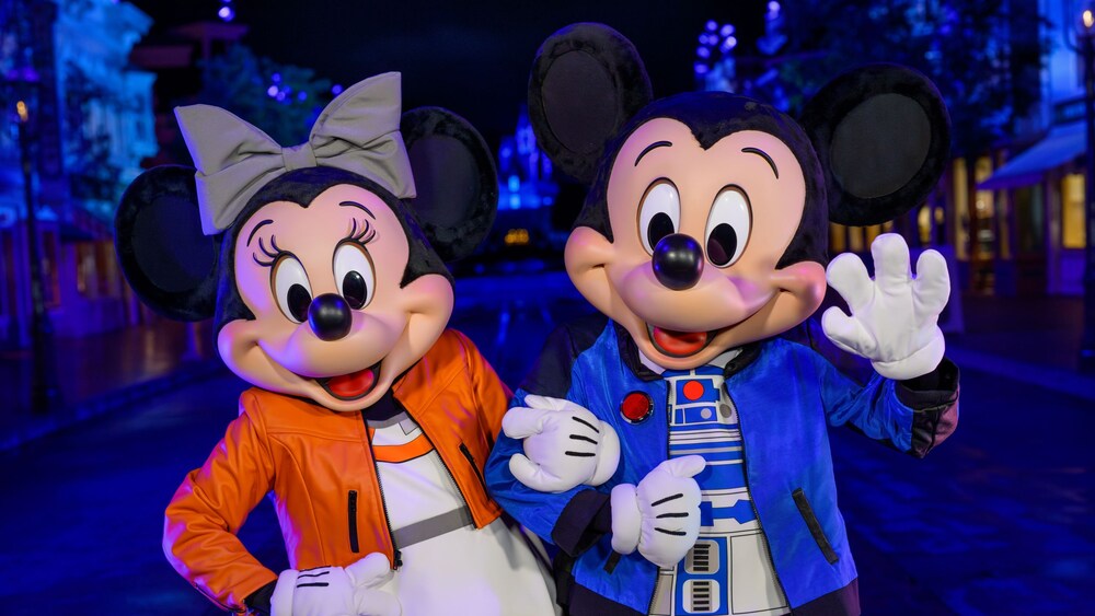 Minnie Mouse wearing a Rebel pilot inspired outfit and Mickey Mouse dressed in an R2 D2 themed jacket at night