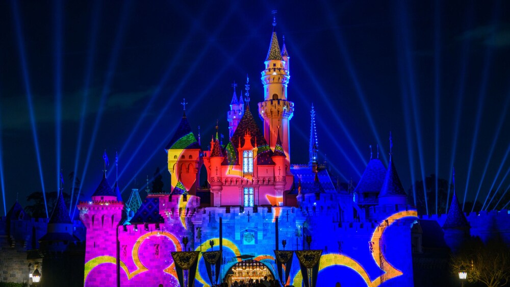 Sleeping Beauty Castle illuminated at night with projections featuring the Disney Channel logo