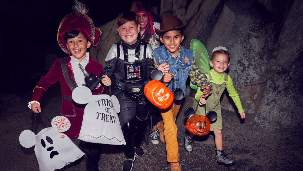 Children dressed up in Halloween costumes carrying ghost-themed bags and plastic pumpkins to collect treats at Oogie Boogie Bash, A Disney Halloween Party.