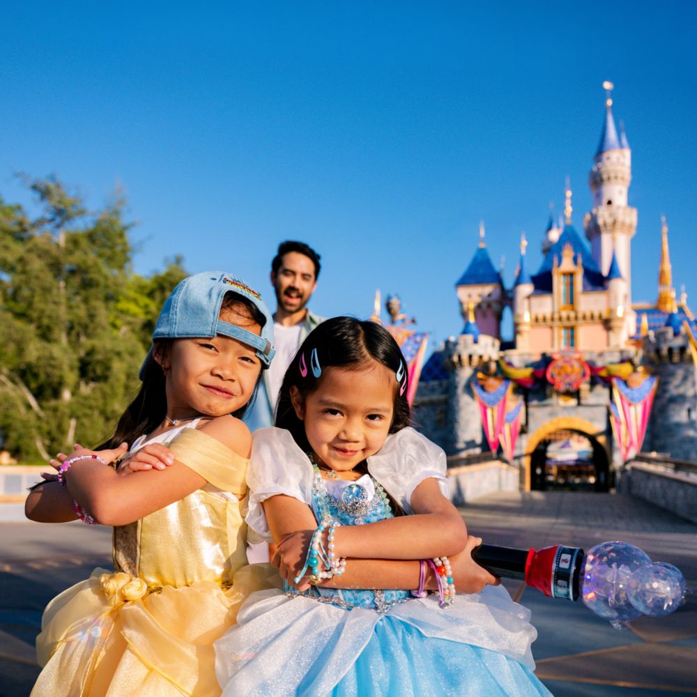 Two young girls in Disney Princess dresses strike a pose in front of Sleeping Beauty Castle at Disneyland Park
