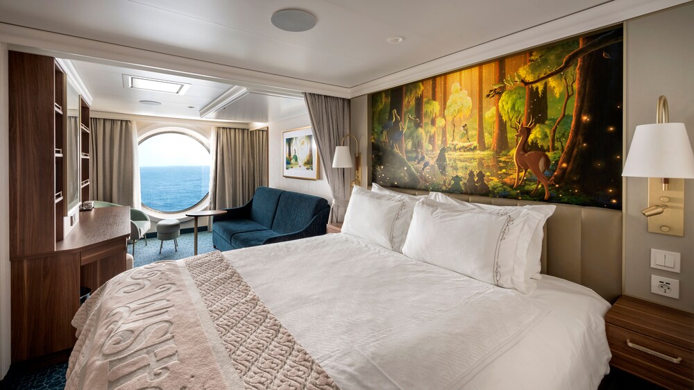 A stateroom with a bed, TV, privacy curtains, a bunkbed, a vanity with mirror and a porthole window