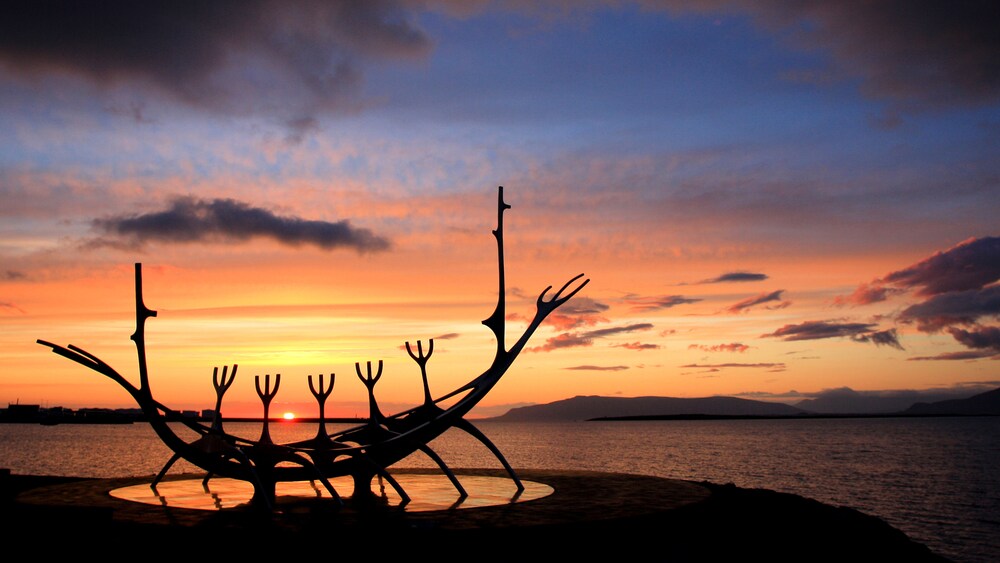 A silhouette of a stylized Viking ship sculpture on a coastline in Reykjavik, Iceland during a sunset