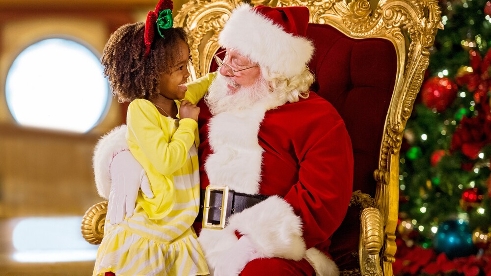 A small girls sits on Santa’s lap and smiles while looking into his eyes