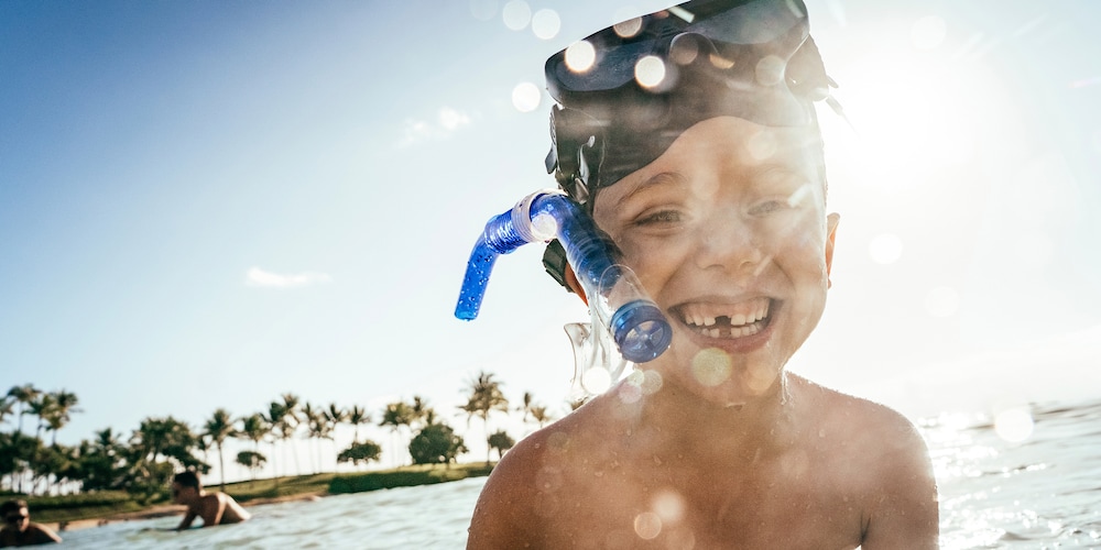 A smiling young boy in shallow ocean water, his snorkeling mask worn high on his forehead