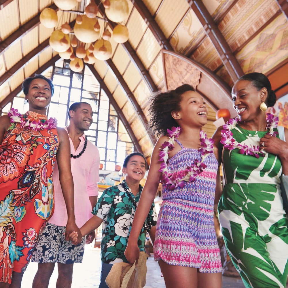 A multi-generational family smile and laugh as they walk through the main lobby at Aulani Resort wearing flower and kukui nut leis