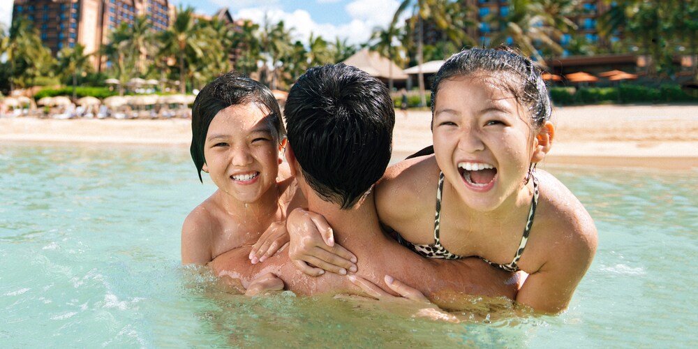 A family plays in the water at a beach nearby a hotel building