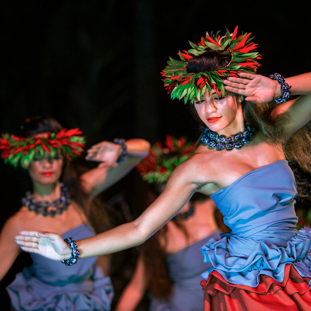A group of Hawaiian women in traditional outfits and leafy head dresses perform an island dance at the Ka Wa'a Luau