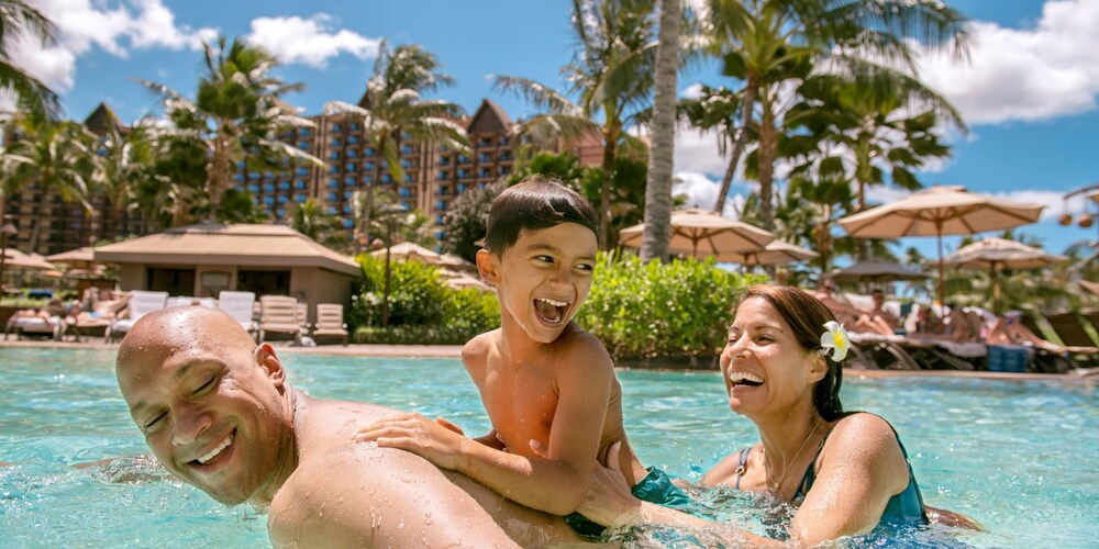 A family of three smiles and laughs as they play in pool flanked by palm trees.