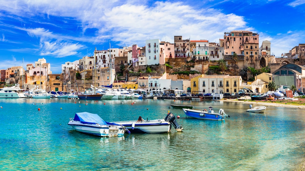 イタリアのシチリア州にあるカステッランマーレ・デル・ゴルフォの海岸沿いに立つ美しい建物と海に浮かぶボート