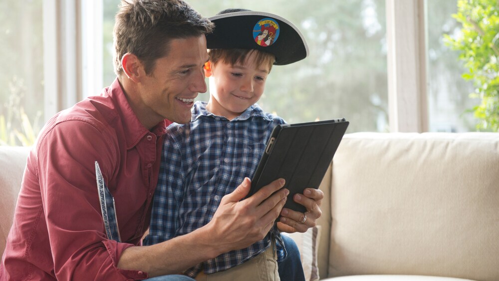 フック船長の海賊の帽子をかぶり、お父さんと一緒にモバイル端末の画面を見る男の子