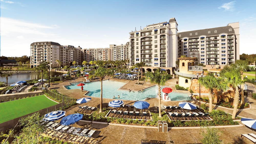 Disney’s Riviera Resort – On Sale Now An outdoor pool with a waterslide, surrounded by lounge chairs, umbrellas and palm trees at Disney's Riviera Resort