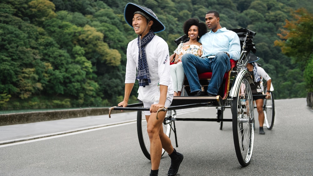 A man and woman riding in a rickshaw cart near a mountain