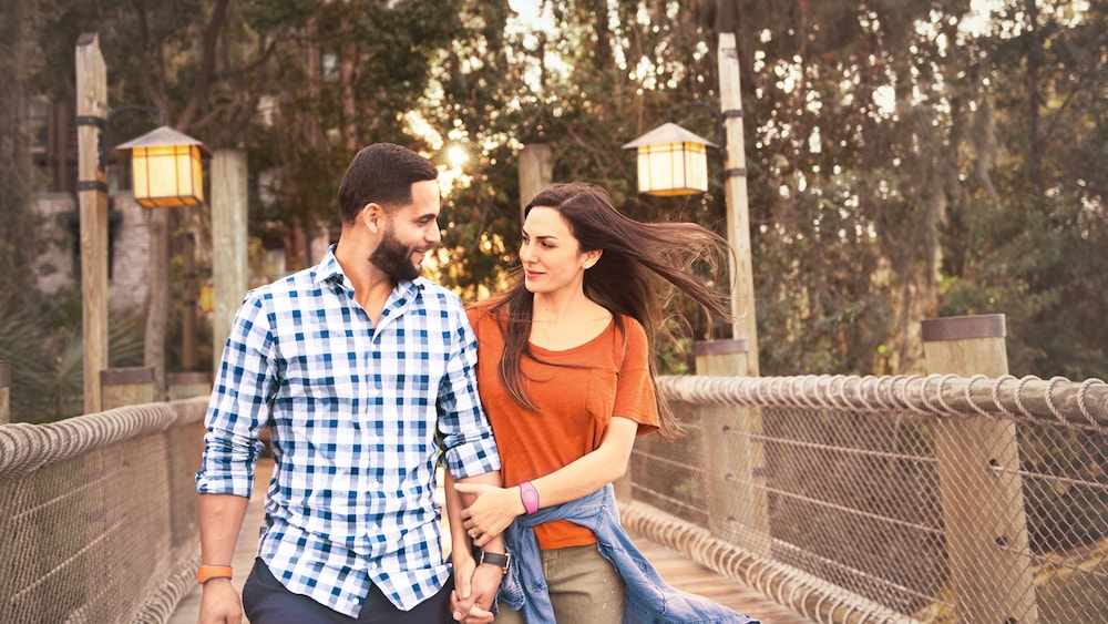 A man and woman holding hands while walking across a bridge