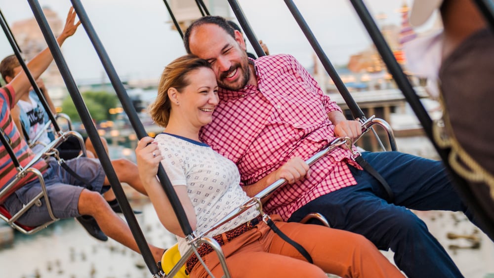 A man and woman sitting in a 2 person swing at Silly Symphony Swings