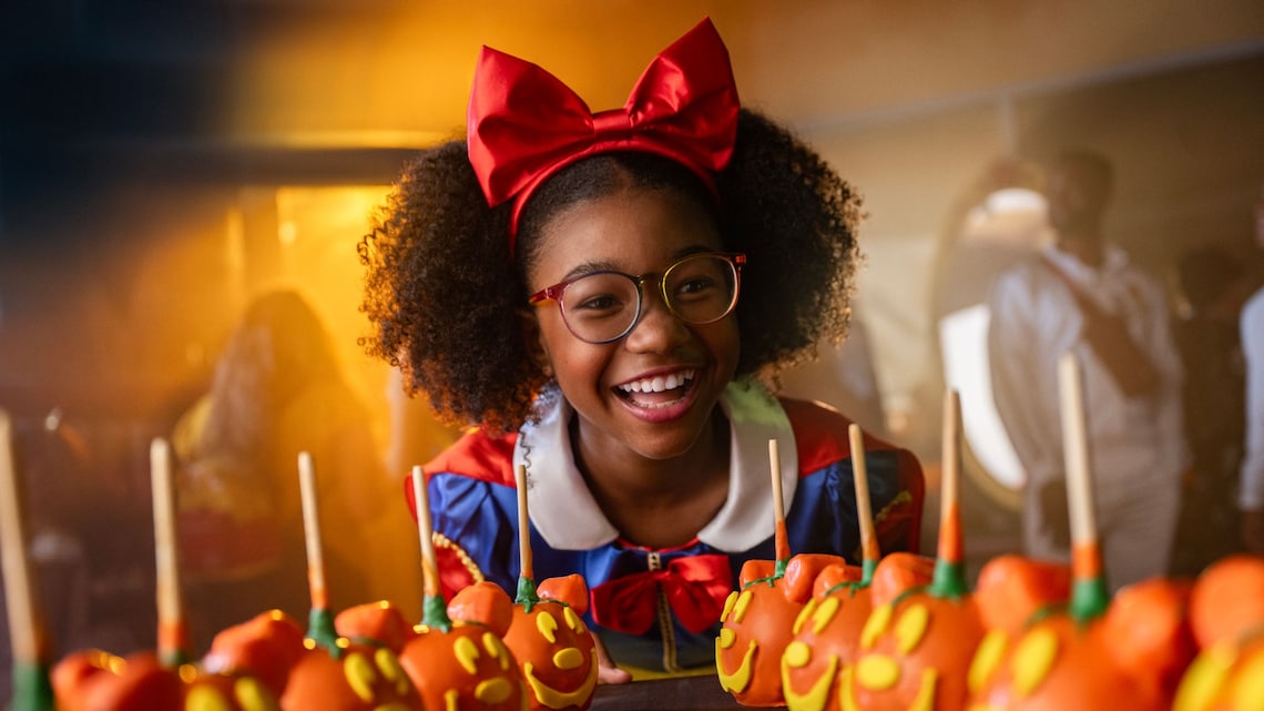 A young girl dressed as Snow White smiling at an array of Mickey Jack o’ Lantern Candy Apples