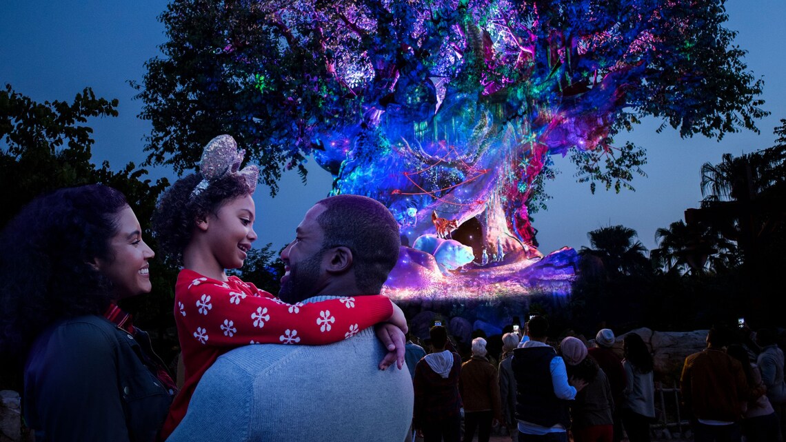 A family of 3 embracing in front of Tree of Life Awakenings Holiday Edition