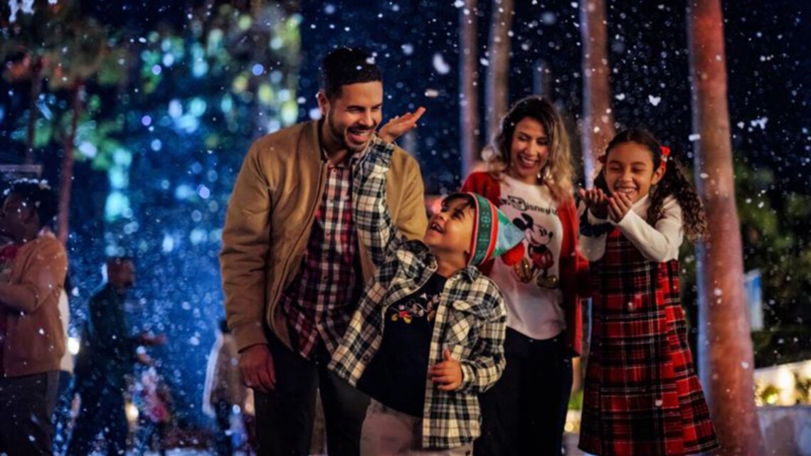 A family of 4 smiling and playing with snow on Main Street USA during Mickey's Very Merry Christmas Party in Magic Kingdom park 