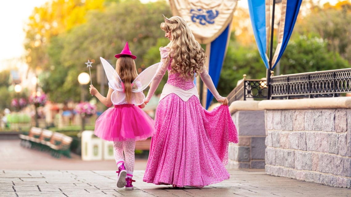 Una niña vestida con un disfraz de hada caminando de la mano con la Princesa Aurora