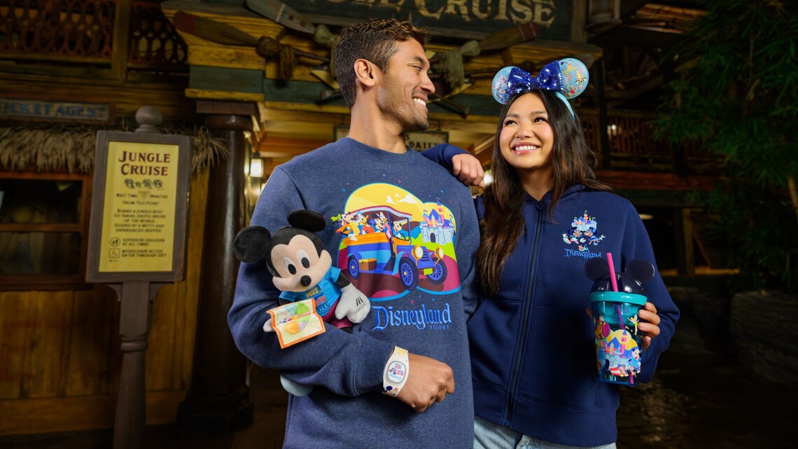 A couple wearing Disneyland Resort apparel holding a Mickey Mouse plush doll and a Disneyland drink tumbler