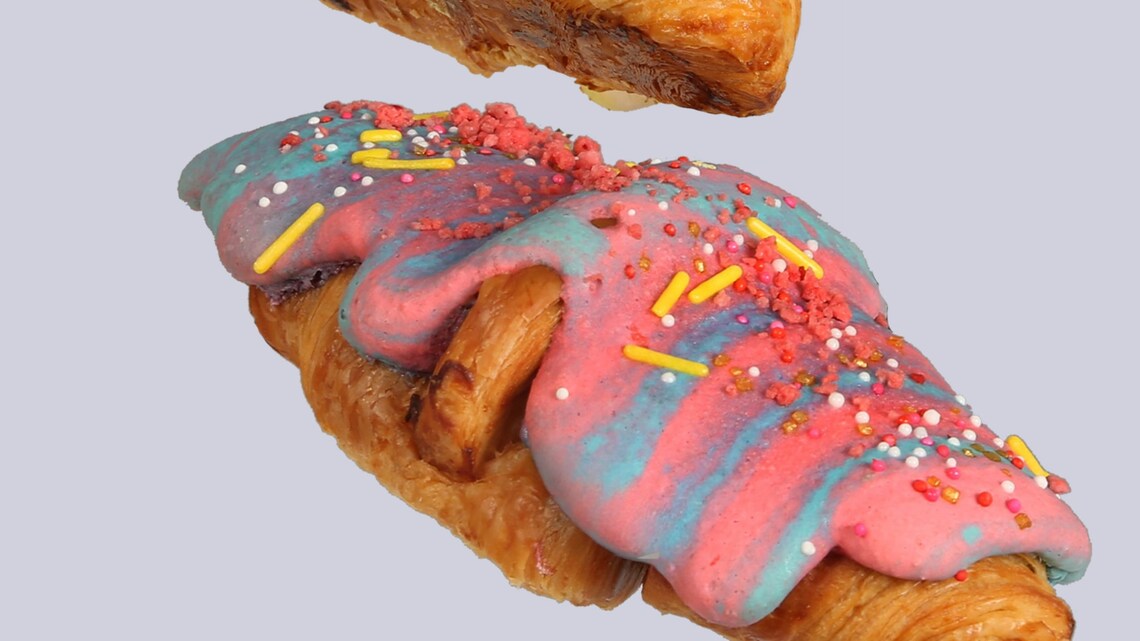 A sign reading Macaron Croissant, Kayla’s Cake depicting 3 different croissants topped with macaron batter