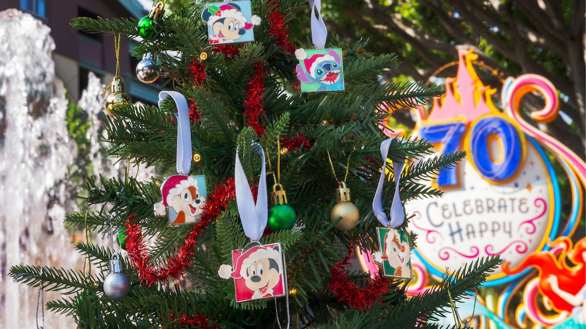 Un árbol de Navidad con adornos de Personajes de Disney junto a un letrero de la Celebración del 70.º Aniversario del Disneyland Resort