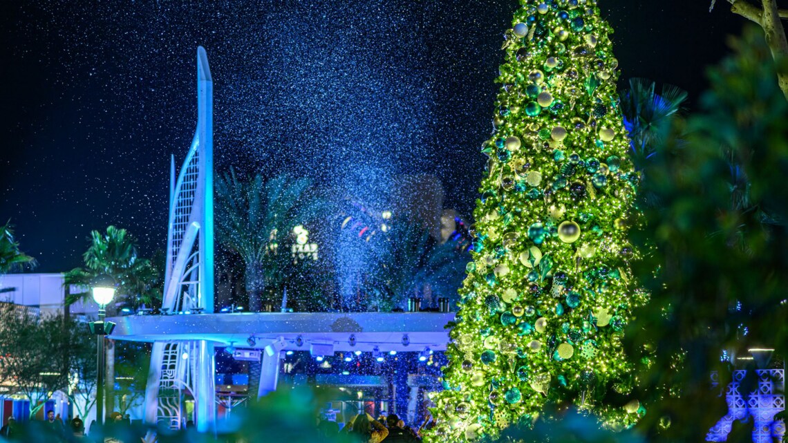 Nieve que vuela por el aire y cae sobre Downtown Disney District junto a un enorme árbol de Navidad decorado