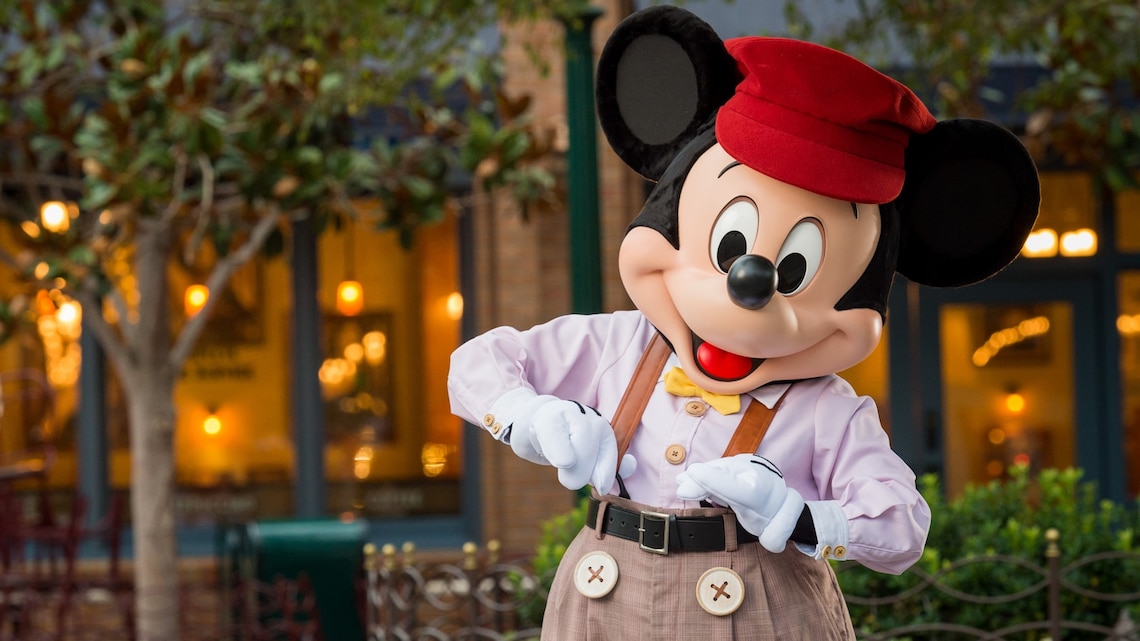 Mickey vestido con pantalones, una camisa abotonada, una corbata de moño, suspensores y una gorra.