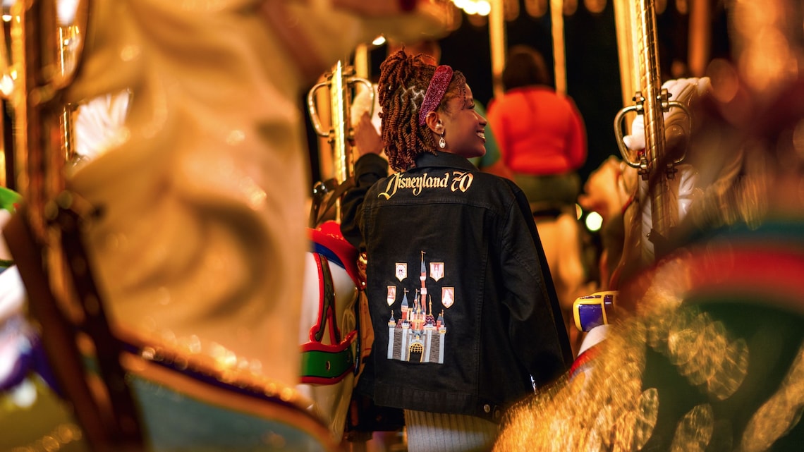 Un Visitante en la atracción King Arthur Carrousel con una chamarra de la Celebración del 70.º Aniversario del Disneyland Resort