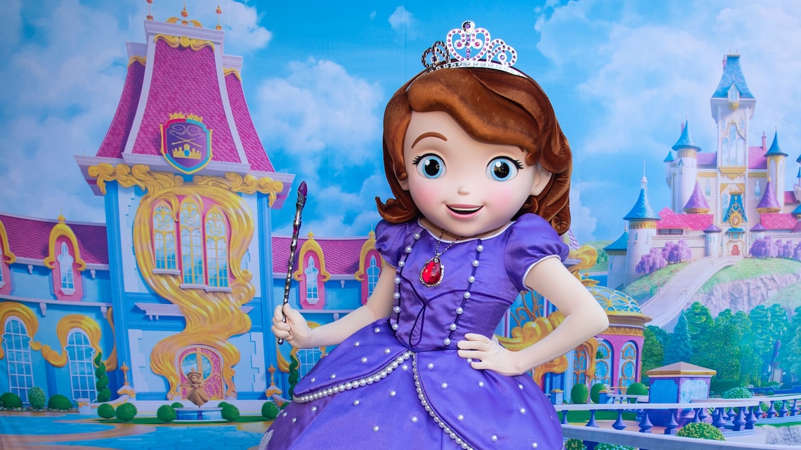 Princess Sofia wearing a dress and crown while holding a wand in front of a castle backdrop