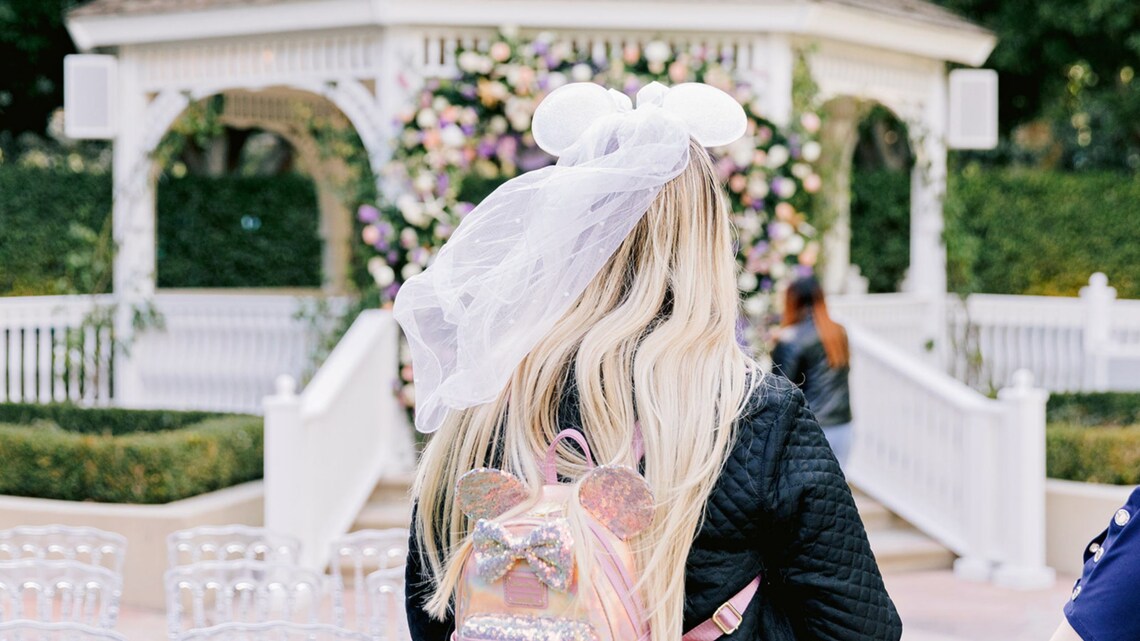 A bride wearing a Minnie Mouse ear headband with a veil while standing near a wedding gazebo 