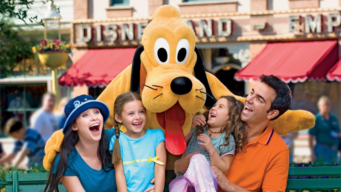 Pluto posing with a family on a bench in front of the Disneyland Emporium on Main Street, U S A