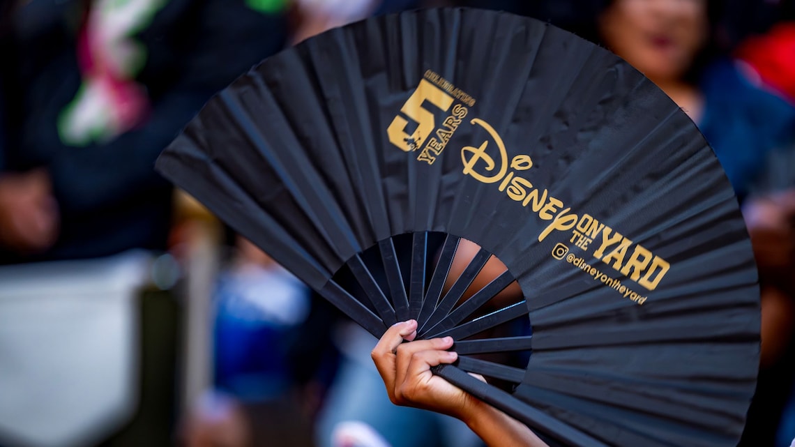 Hand holding a commemorative paper fan from Disney on the Yard's 5 year celebration