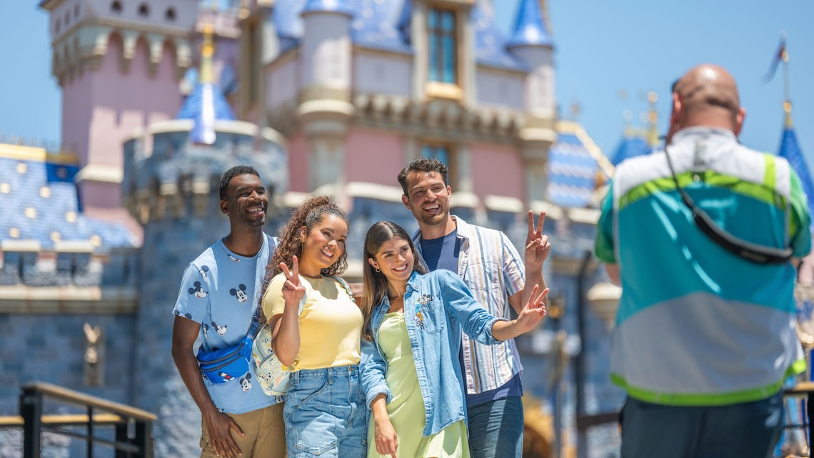 A man taking a photo of 4 Guests posing in front of Sleeping Beauty Castle