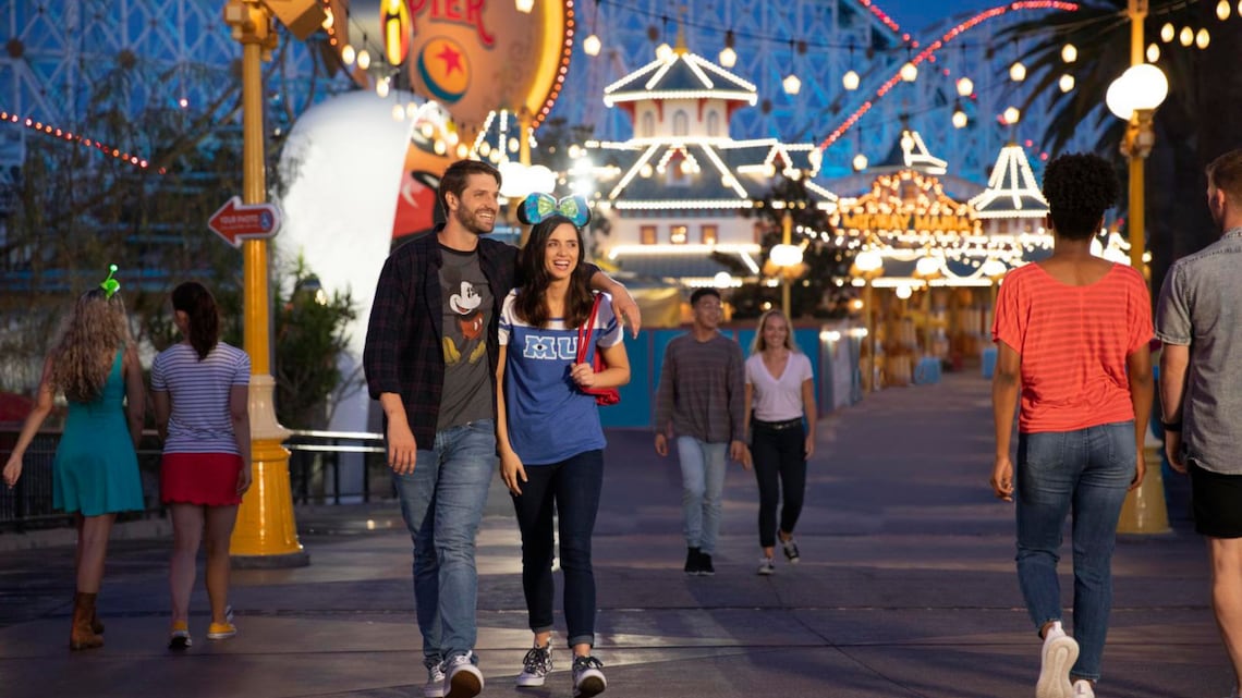 Visitantes caminando por Pixar Pier mientras está encendido por la noche