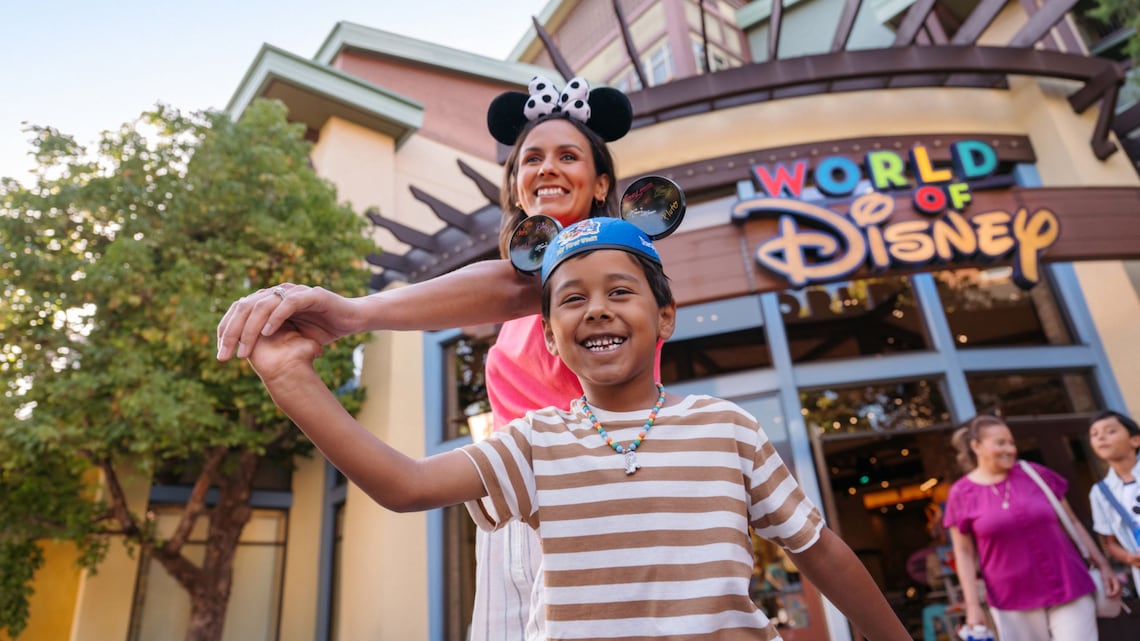 A mother and son holding hands and wearing Mickey Mouse and Minnie mouse ear hats outside of World of Disney at Downtown Disney District