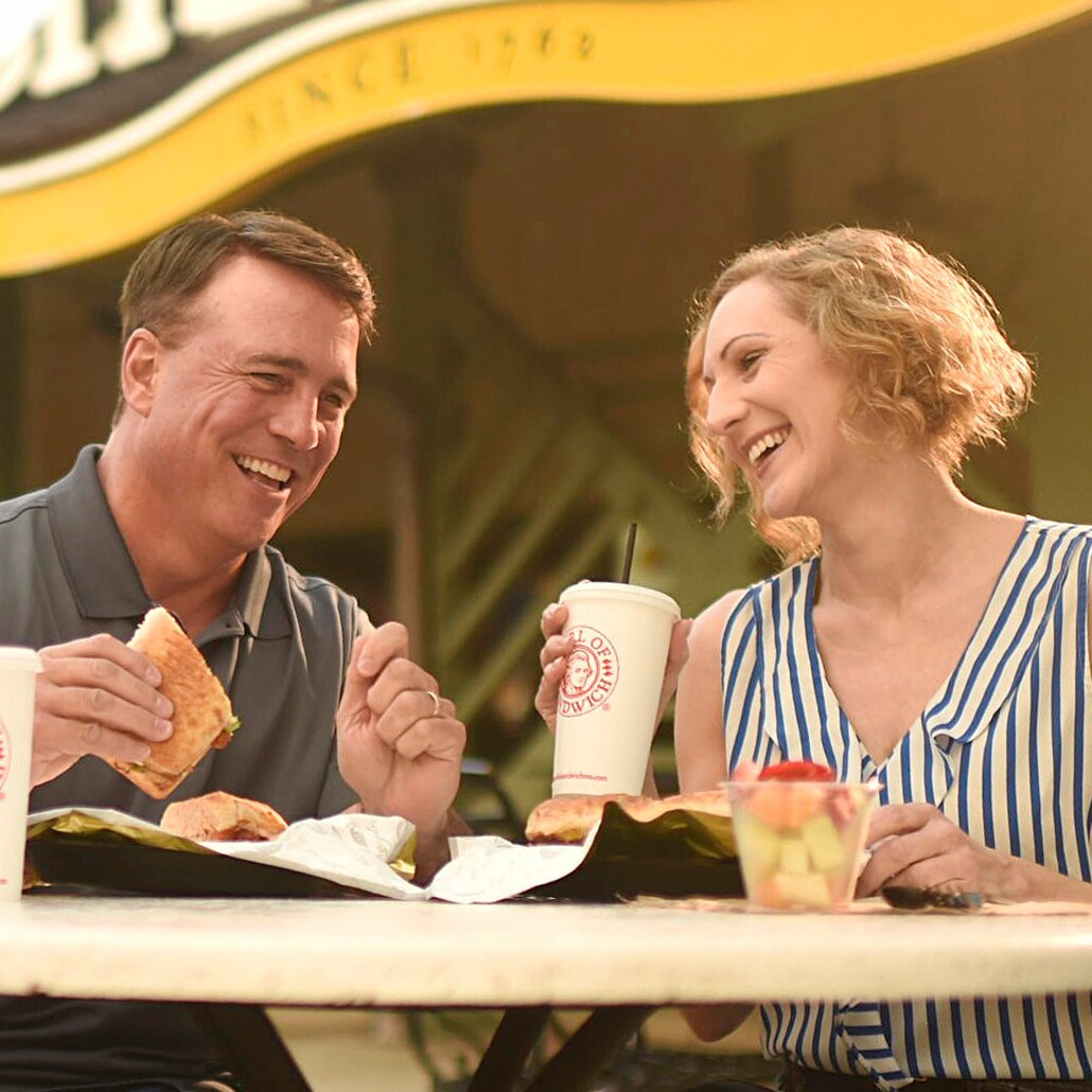 A couple sits at an outdoor table enjoying their Earl of Sandwich meals