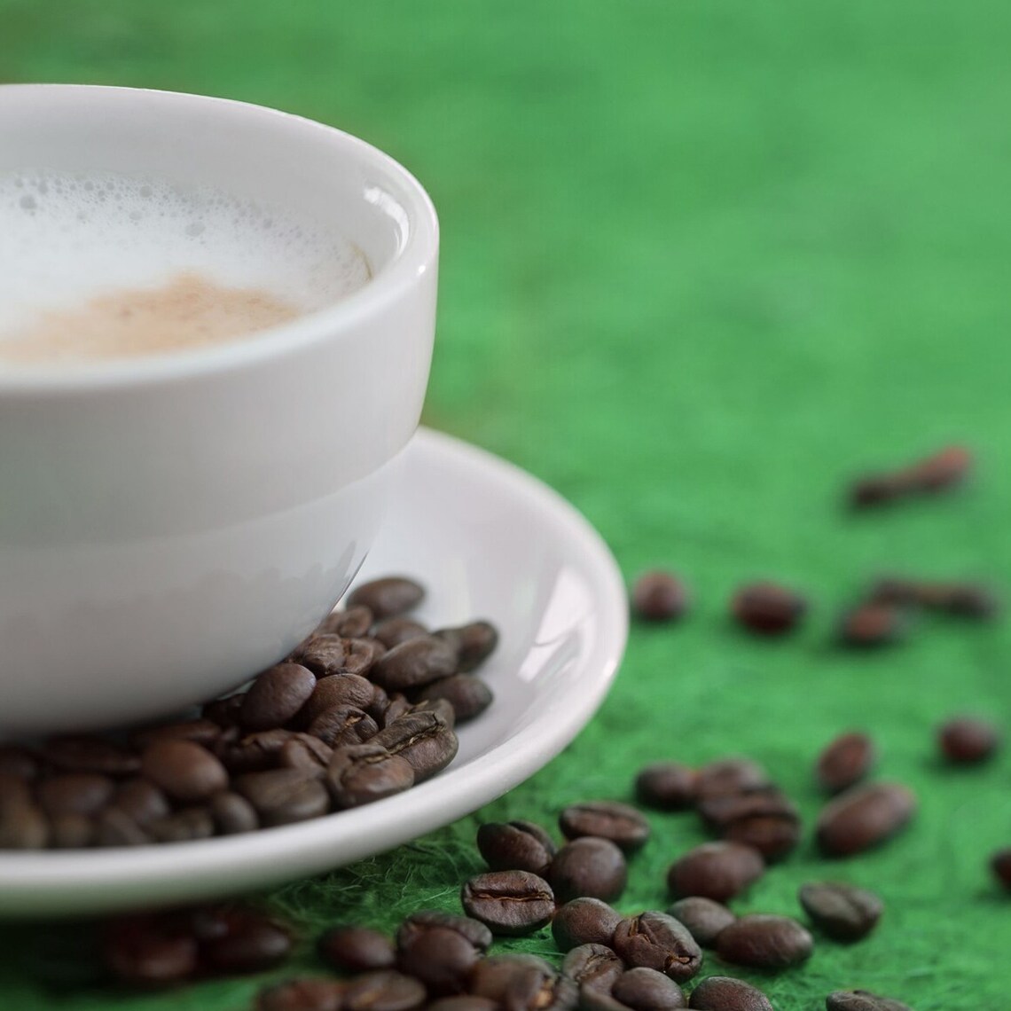 A foamy cup of cappuccino from Starbucks plated beside a scattered array of espresso beans