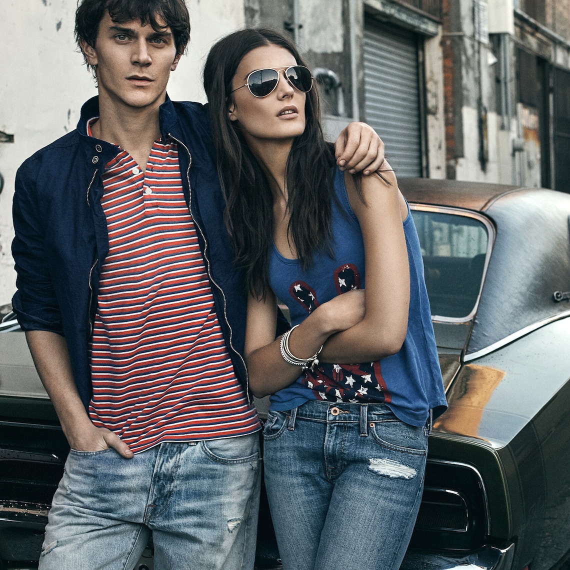 A couple wearing Lucky Brand apparel leans against the trunk of a vintage car in an alley