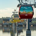 People ride the Disney Skyliner over a body of water near a bridge