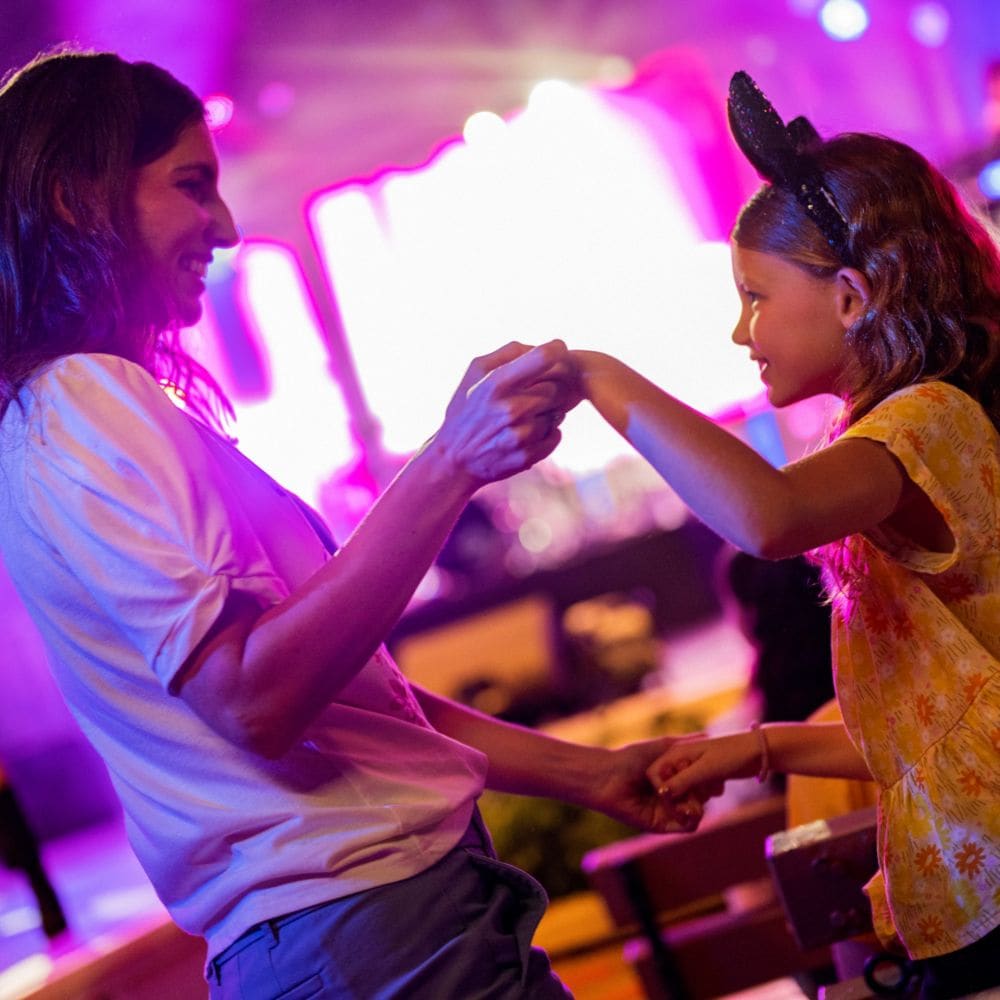 A woman and girl dancing together in a concert venue with a performer on stage