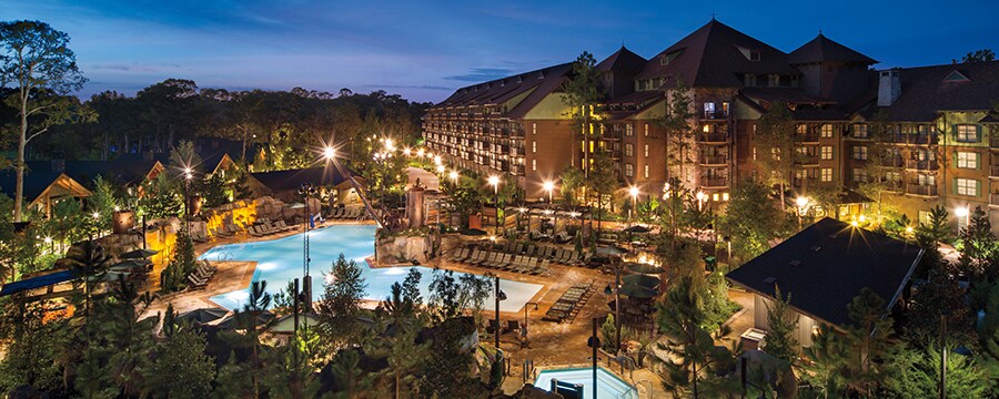 Alpine trees surrounding a multistory wood and stone wilderness lodge with an impressive pool area 