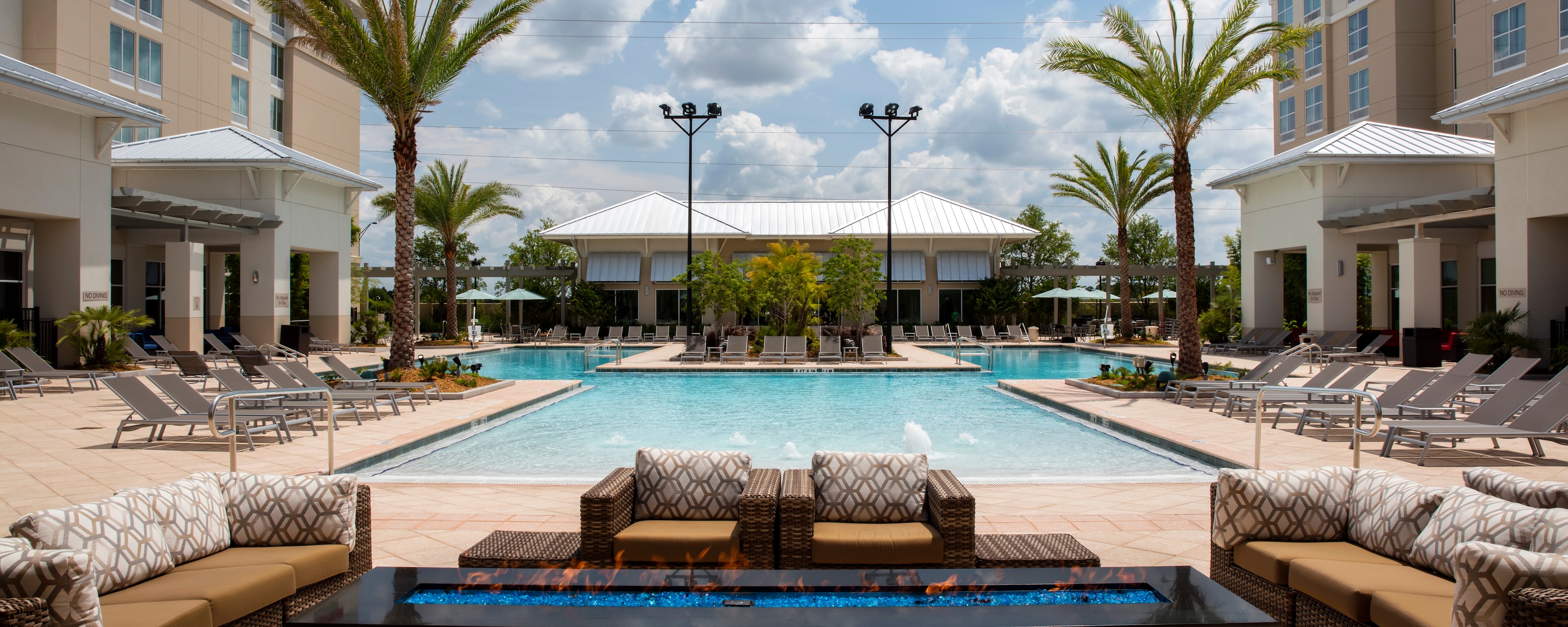 A swimming pool with outdoor recliners, a firepit and stylish outdoor couches